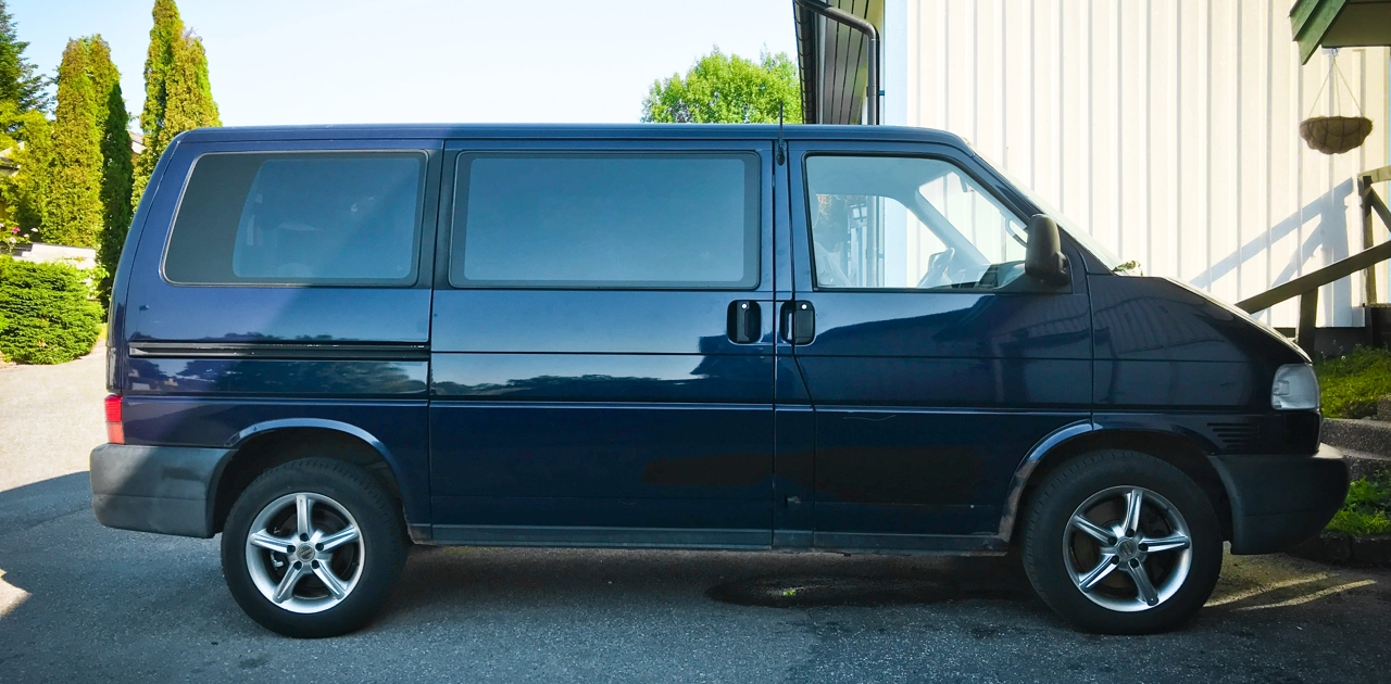 Dark blue VW Caravelle parked next to white and blue house