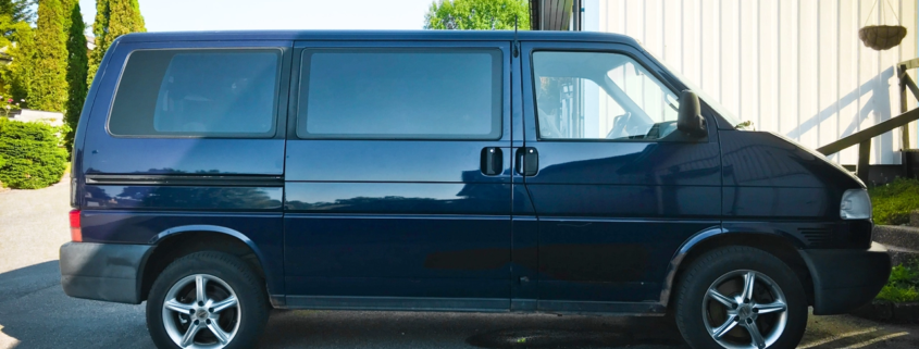 Dark blue VW Caravelle parked next to white and blue house