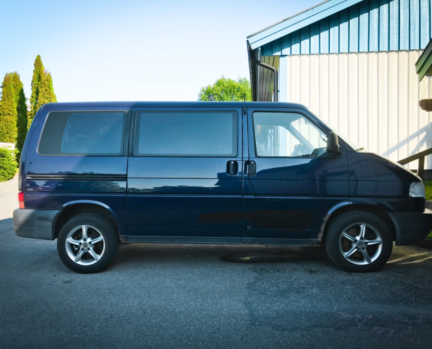 Dark blue VW Caravelle parked next to white and blue house